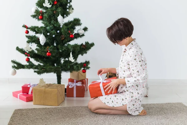 Ευτυχισμένη γυναίκα που ανοίγει χριστουγεννιάτικα δώρα. Χριστουγεννιάτικο δέντρο με δώρα από κάτω. Διακοσμημένο σαλόνι — Φωτογραφία Αρχείου