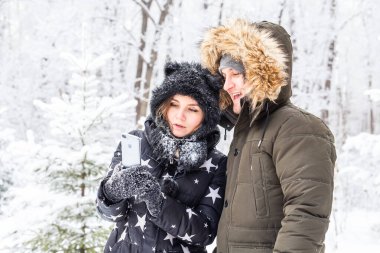 Teknoloji ve ilişki konsepti mutlu bir çiftin kış ormanında selfie çekmesi.