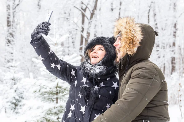 Saison, amour, technologie et concept de loisirs - couple heureux prenant selfie par smartphone sur fond d'hiver — Photo
