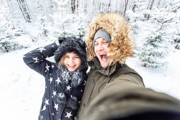Tecnologias e conceito de relacionamento - Feliz casal sorrindo tirar uma selfie em uma floresta de inverno fora — Fotografia de Stock