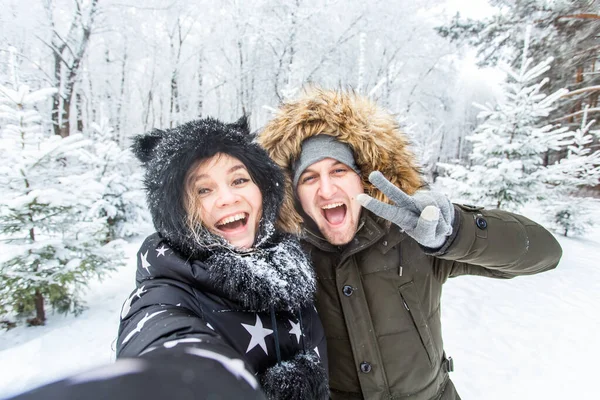 季節、愛、技術、レジャーのコンセプト-幸せなカップルは冬の背景にスマートフォンで自撮り — ストック写真