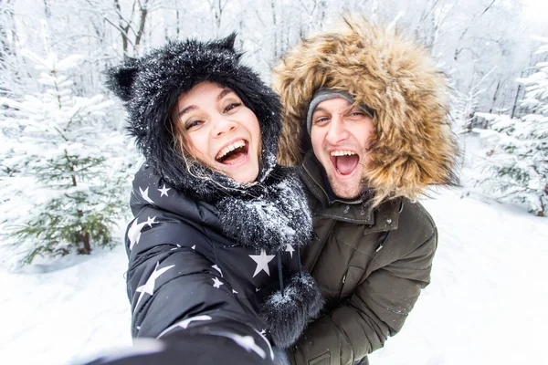 Teknoloji ve ilişki konsepti mutlu bir çiftin kış ormanında selfie çekmesi. — Stok fotoğraf