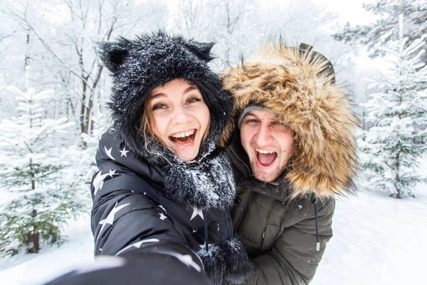 Temporada, amor, tecnología y concepto de ocio - pareja feliz tomando selfie por teléfono inteligente sobre fondo de invierno —  Fotos de Stock