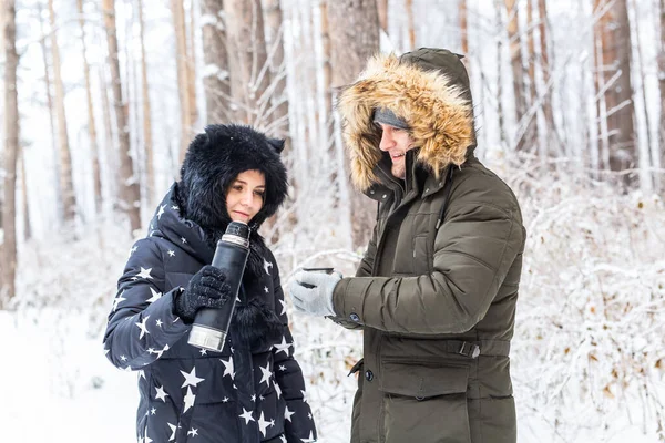 O par jovem no amor bebe uma bebida quente de uma garrafa térmica e gosta da natureza de inverno. — Fotografia de Stock