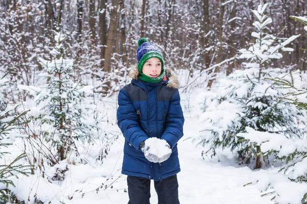 Милый мальчик играет со снегом, веселится, улыбается. Подросток в зимнем парке. активный образ жизни, зимняя активность, открытый зимний игры, снежки. — стоковое фото