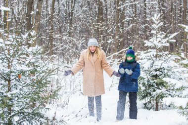 Eğlence ve mevsim konsepti - Mutlu anne ve oğul kış ormanlarında karla oynayıp eğleniyorlar