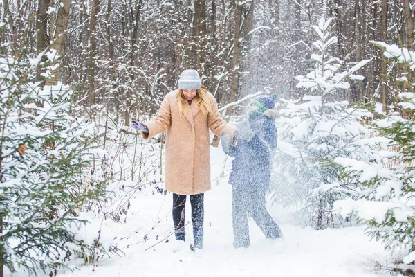 Концепція веселощів і сезону Щаслива мати і син розважаються і грають зі снігом в зимовому лісі — стокове фото