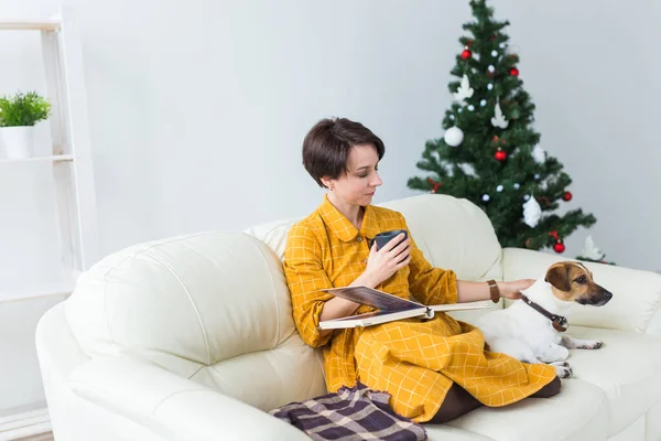 Karácsony, ünnepek és az emberek koncepció - boldog fiatal nő olvasás könyv otthon. — Stock Fotó