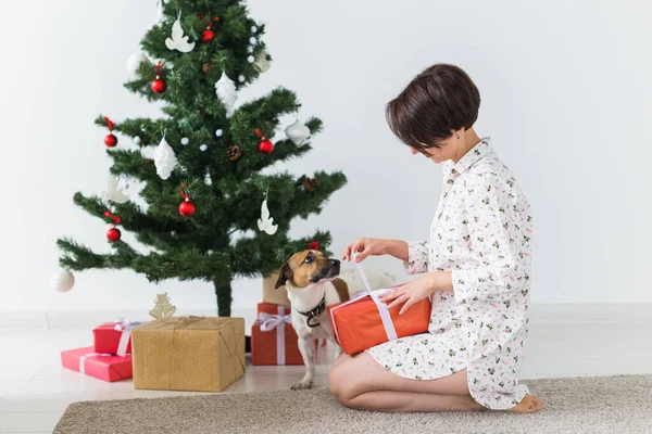 Gelukkige vrouw met hond die kerstcadeaus opent. Kerstboom met cadeautjes eronder. Ingerichte woonkamer — Stockfoto