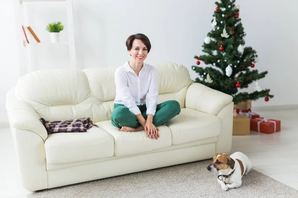 Joyeux jeune femme avec beau chien dans le salon avec arbre de Noël. Concept de vacances. — Photo