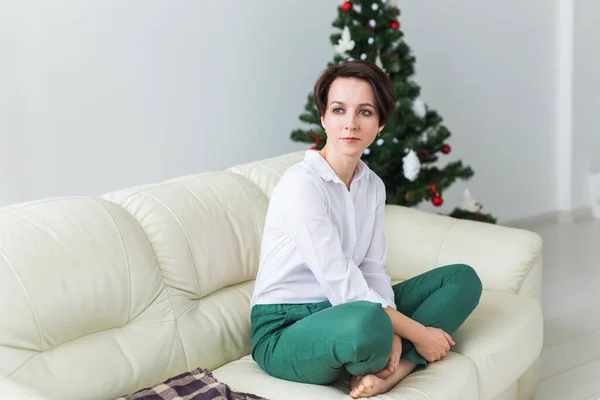 Щаслива молода жінка на дивані у вітальні з ялинкою. концепція відпустки . — стокове фото
