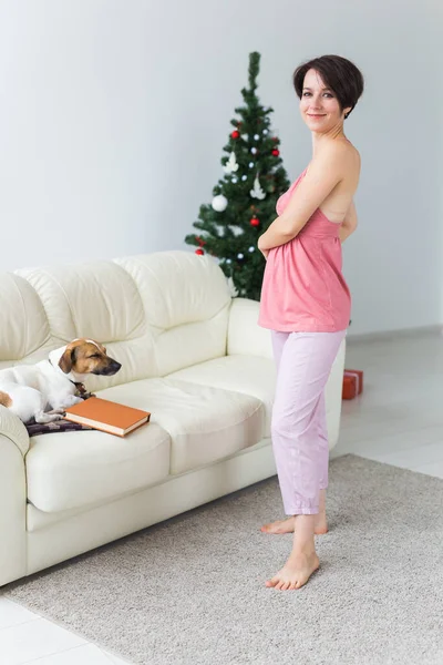 Gelukkige jonge vrouw met mooie hond in woonkamer met kerstboom. Vakantieconcept. — Stockfoto