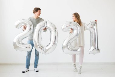 Tatiller, şenlik ve parti konsepti mutlu çift, beyaz arka planda gümüş 2021 balon tutuyor. Yeni yıl kutlaması.