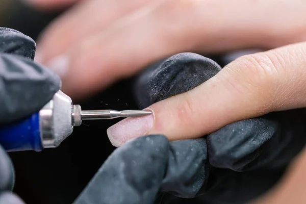 Un primo piano di manicure hardware in un salone di bellezza. Manicurista sta applicando la lima elettrica trapano per unghie per manicure sulle dita femminili. — Foto Stock