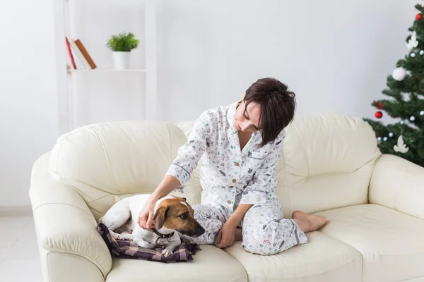 Joyeux jeune femme en pyjama avec beau chien dans le salon avec arbre de Noël. Concept de vacances. — Photo