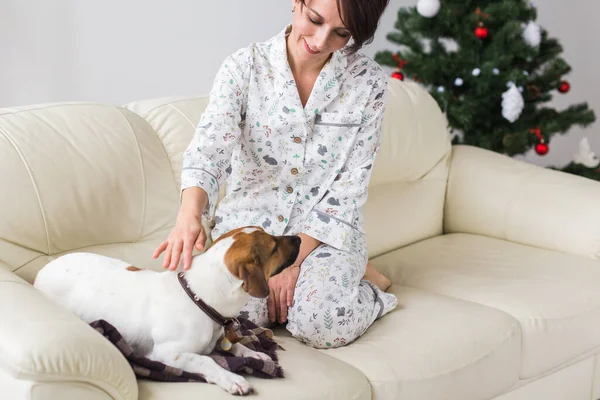 Szczęśliwa młoda kobieta w piżamie z uroczym psem w salonie z choinką. Koncepcja urlopu. — Zdjęcie stockowe