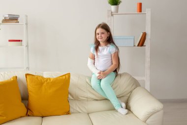 Kırık bileği ya da kolu olan bir çocuk gülümsüyor ve kanepede eğleniyor. Pozitif tutum, iyileşme ve çocuk konsepti.