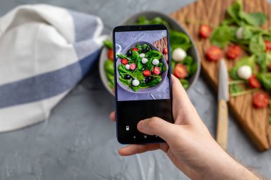 Mozarella ve cep telefonu kamerasında ıspanak ile taze sebze salatası çeken bir adam. Yemek pişirme, blog yazma ve sağlıklı beslenme kavramı.