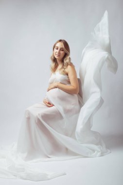 Uçan beyaz kumaş giyen zarif hamile bir genç kadın. Hamilelik, annelik ve annelik kavramı.