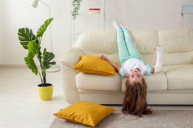 Kırık bileği ya da kolu olan bir çocuk gülümsüyor ve kanepede eğleniyor. Pozitif tutum, iyileşme ve çocuk konsepti.