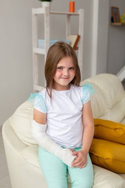 Kırık bileği ya da kolu olan bir çocuk gülümsüyor ve kanepede eğleniyor. Pozitif tutum, iyileşme ve çocuk konsepti.