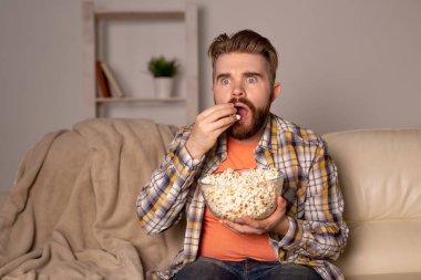 Sakallı adam film ya da spor oyunları seyrediyor. Geceleri evde patlamış mısır yiyor. Sinema, şampiyonluk ve eğlence konsepti.