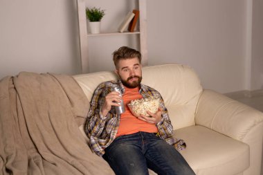 Sakallı adam film ya da spor oyunları seyrediyor. Geceleri evde patlamış mısır yiyor. Sinema, şampiyonluk ve eğlence konsepti.