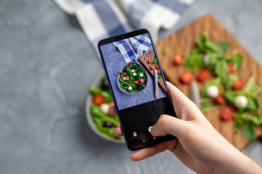 Mozarella ve cep telefonu kamerasında ıspanak ile taze sebze salatası çeken bir adam. Yemek pişirme, blog yazma ve sağlıklı beslenme kavramı.