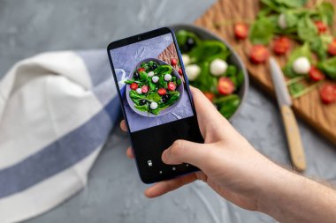 Mozarella ve cep telefonu kamerasında ıspanak ile taze sebze salatası çeken bir adam. Yemek pişirme, blog yazma ve sağlıklı beslenme kavramı.