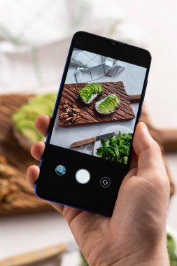 Eller, masada duran iki güzel sağlıklı ekşi krema ve avokado sandviçinin resimlerini akıllı telefondan çeker. Sosyal medya ve gıda kavramı