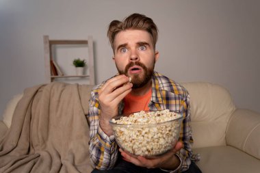 Sakallı adam film ya da spor oyunları seyrediyor. Geceleri evde patlamış mısır yiyor. Sinema, şampiyonluk ve eğlence konsepti.