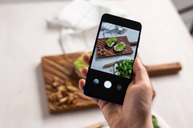 Eller, masada duran iki güzel sağlıklı ekşi krema ve avokado sandviçinin resimlerini akıllı telefondan çeker. Sosyal medya ve gıda kavramı