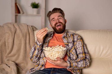 Sakallı adam film ya da spor oyunları seyrediyor. Geceleri evde patlamış mısır yiyor. Sinema, şampiyonluk ve eğlence konsepti.