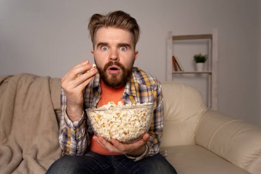 Sakallı adam film ya da spor oyunları seyrediyor. Geceleri evde patlamış mısır yiyor. Sinema, şampiyonluk ve eğlence konsepti.