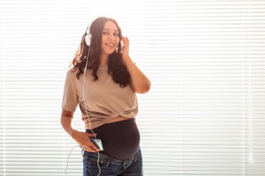 Güzel, genç, huzurlu, hamile bir kadın akıllı telefon ve kulaklık kullanarak hoş klasik müzik dinliyor. Doğumdan önce pozitif tavır kavramı. Boşluğu kopyala