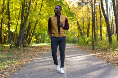 Sıcak, güneşli bir günde, şık giyinmiş Afro-Amerikalı genç adam yaz parkında yürüyor. Açık hava etkinliği kavramı.