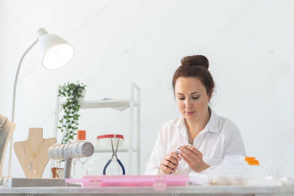 Charming young enthusiastic caucasian woman making beautiful unique costume jewelry while sitting at her desk. Concept of hobby and pleasant work