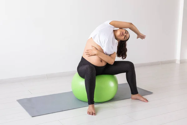 Joven mujer embarazada flexible haciendo gimnasia en la alfombra en el suelo sobre fondo blanco. El concepto de preparar el cuerpo para el parto fácil —  Fotos de Stock