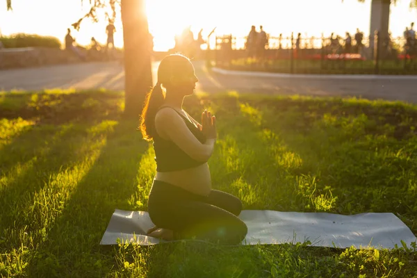 黒いスーツの赤ちゃんを期待している若い女性の側のビューは、ラグ裸足で立って、暖かい晴れた夏の日に瞑想します。スポーツと瞑想活動の概念 — ストック写真