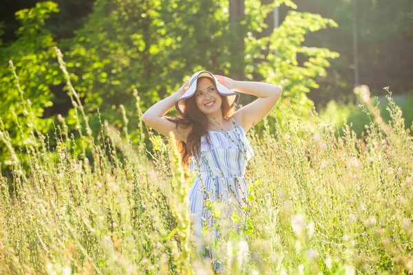 Giovane donna che cammina tra i fiori selvatici nella soleggiata giornata estiva. Concetto della gioia di comunicare con la natura estiva — Foto Stock