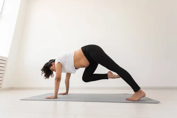Joven mujer embarazada flexible haciendo gimnasia en la alfombra en el suelo sobre fondo blanco. El concepto de preparar el cuerpo para el parto fácil —  Fotos de Stock