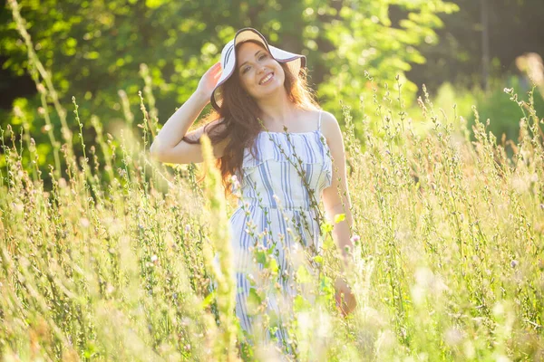 Giovane donna che cammina tra i fiori selvatici nella soleggiata giornata estiva. Concetto della gioia di comunicare con la natura estiva — Foto Stock