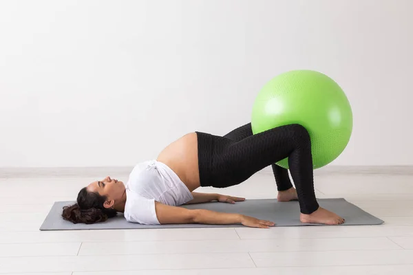 Jovem mulher grávida flexível fazendo ginástica no tapete no chão no fundo branco. O conceito de preparar o corpo para o parto fácil — Fotografia de Stock