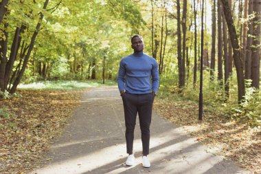 Sıcak, güneşli bir günde, şık giyinmiş Afro-Amerikalı genç adam yaz parkında yürüyor. Açık hava etkinliği kavramı.