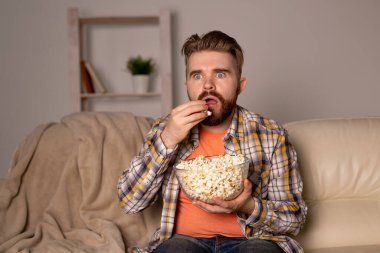 Sakallı adam film ya da spor oyunları seyrediyor. Geceleri evde patlamış mısır yiyor. Sinema, şampiyonluk ve eğlence konsepti.