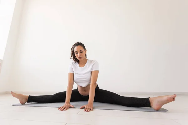 Joven mujer embarazada flexible haciendo gimnasia en la alfombra en el suelo sobre fondo blanco. El concepto de preparar el cuerpo para el parto fácil —  Fotos de Stock