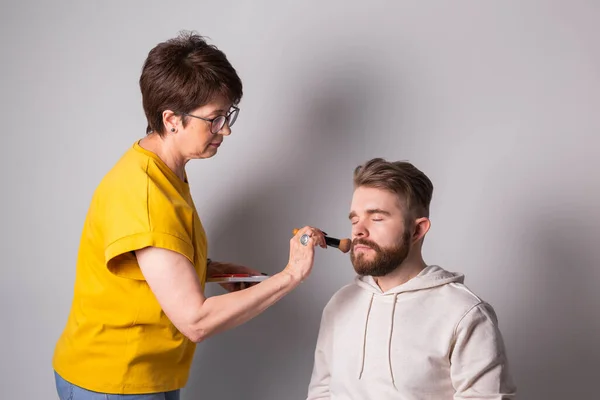 Hombre barbudo maquillándose. Mujer visagista trabaja con cepillo. —  Fotos de Stock