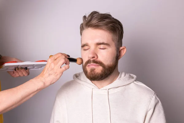 Бородатий чоловік отримує макіяж. Рука візажиста за допомогою пензля . — стокове фото
