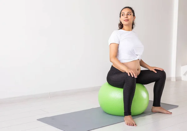 Una joven embarazada haciendo ejercicio de relajación usando una pelota de fitness mientras está sentada en una esterilla. Espacio de copia —  Fotos de Stock