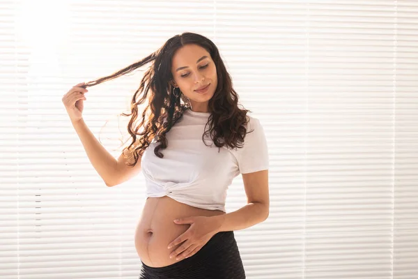 Usmívající se mladá krásná těhotná žena dotýkající se břicha a vlasů a radující se. Pojem zdraví a přemýšlet o budoucnosti při čekání na dítě. Copyspace — Stock fotografie
